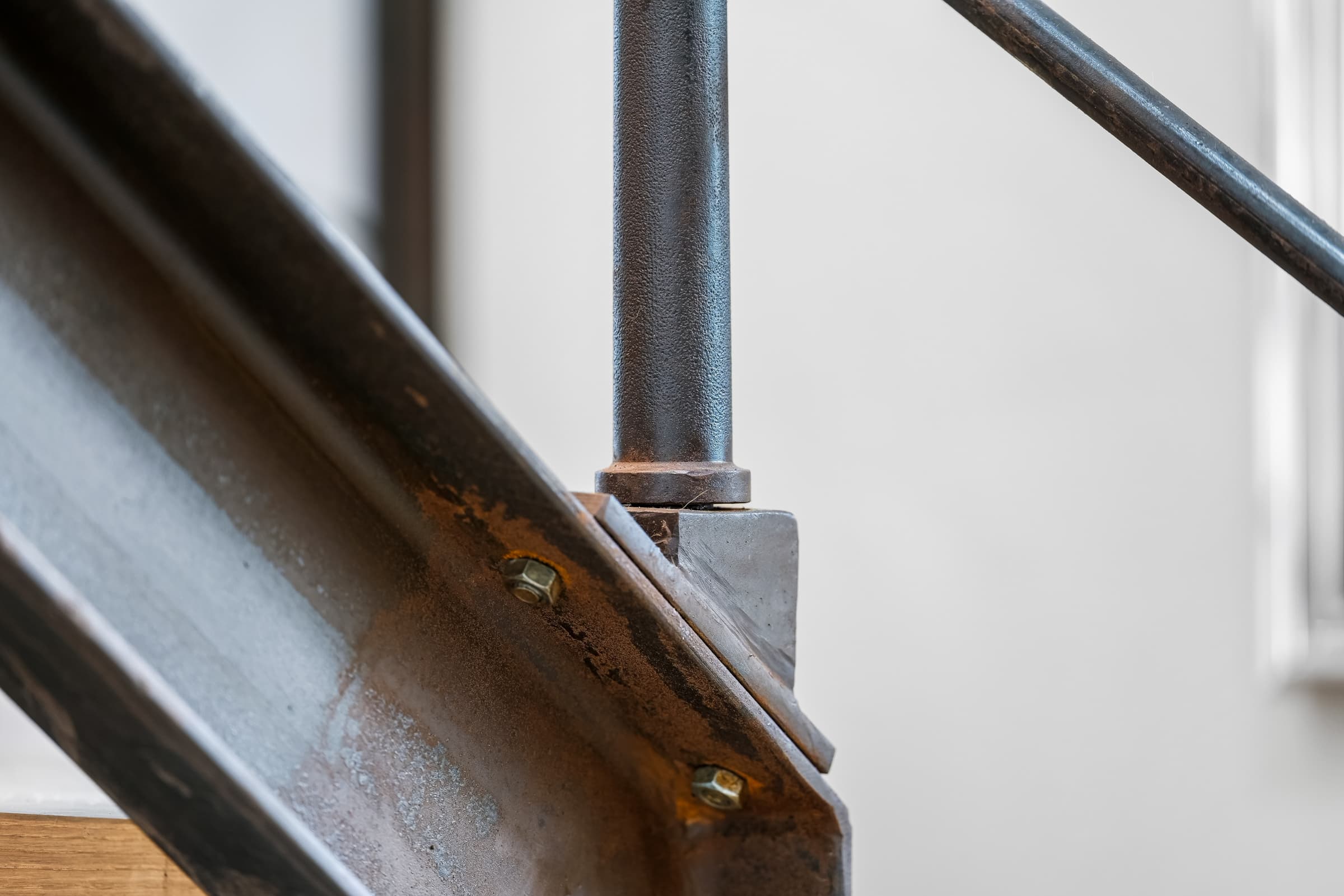 Detal schodów: surowa stal, mosiężne śruby i okrągły pręt balustrady