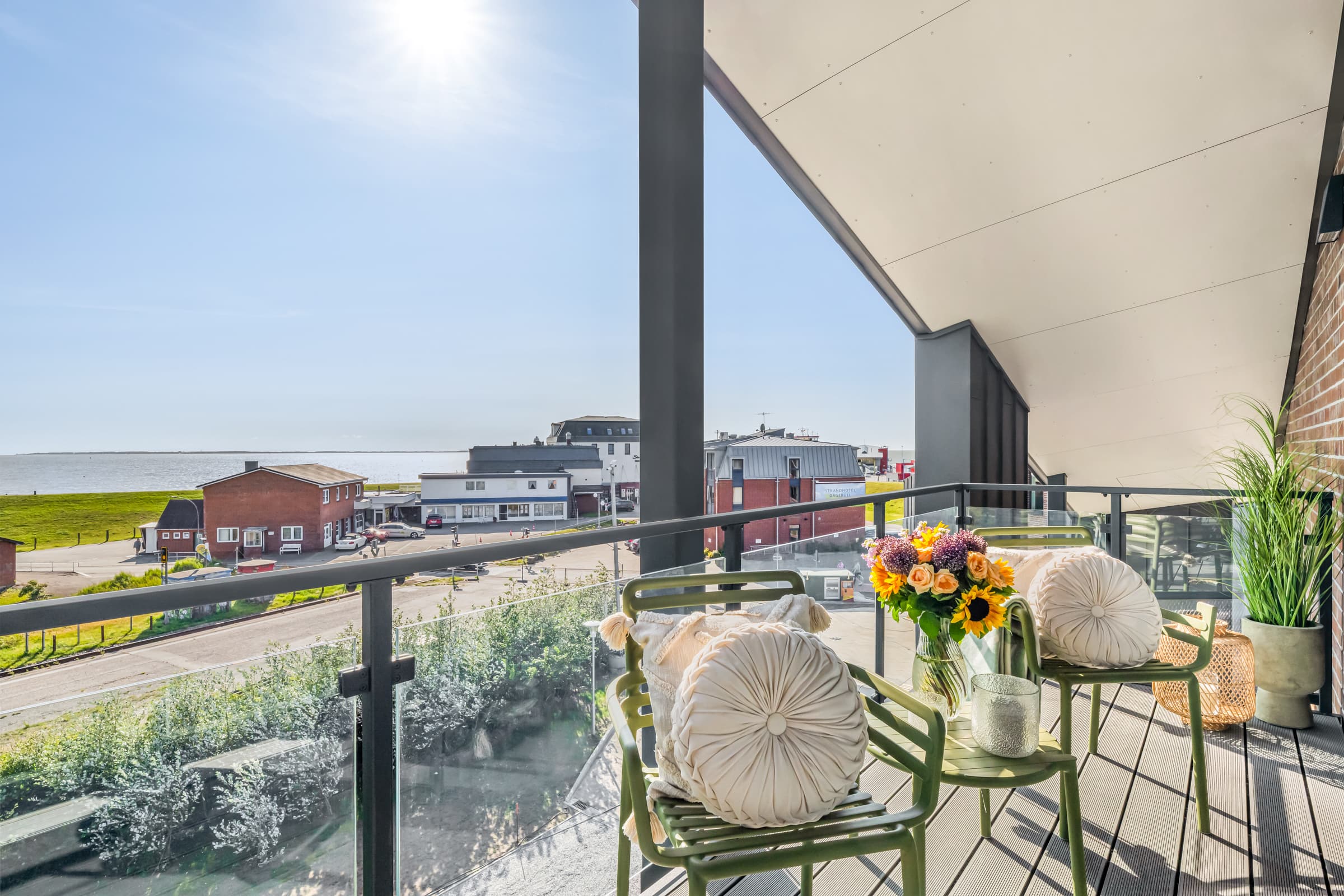 Umeblowany balkon z kwiatami i szklaną balustradą, widok na ulicę portową i Morze Północne