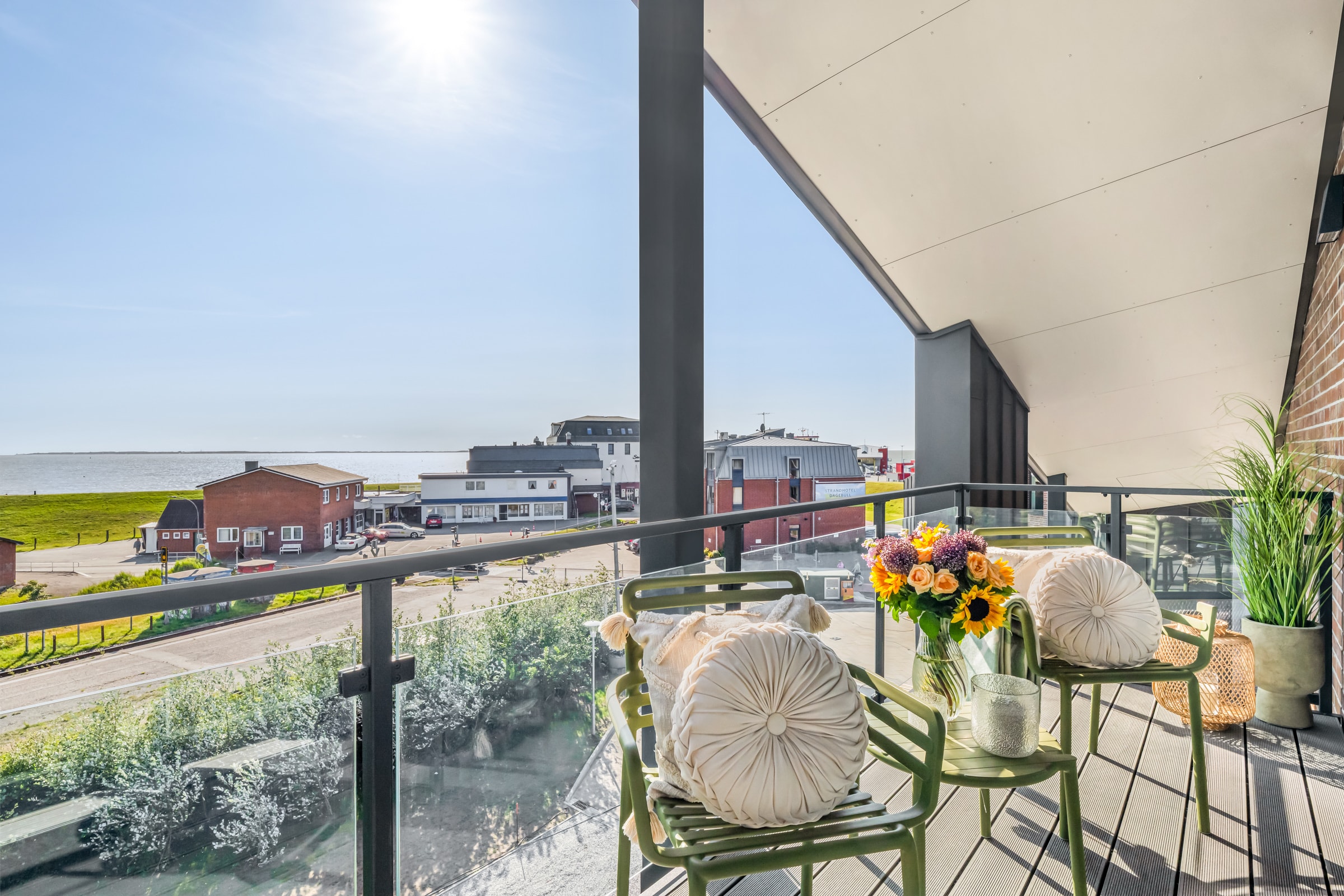 Umeblowany balkon z kwiatami i szklaną balustradą, widok na ulicę portową i Morze Północne