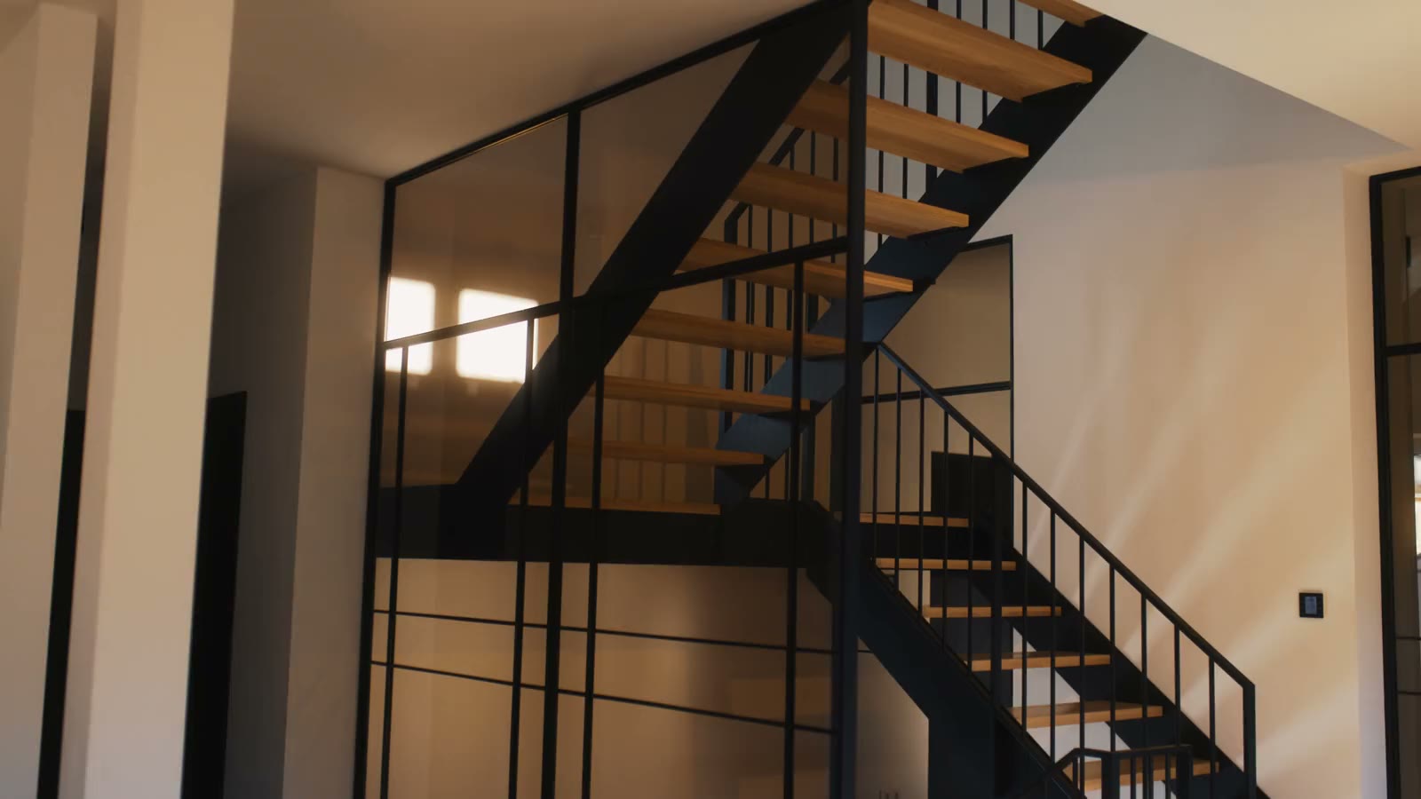 Wieczorne ujęcie drewnianych schodów z czarną balustradą i przeszkleniem ze szprosami