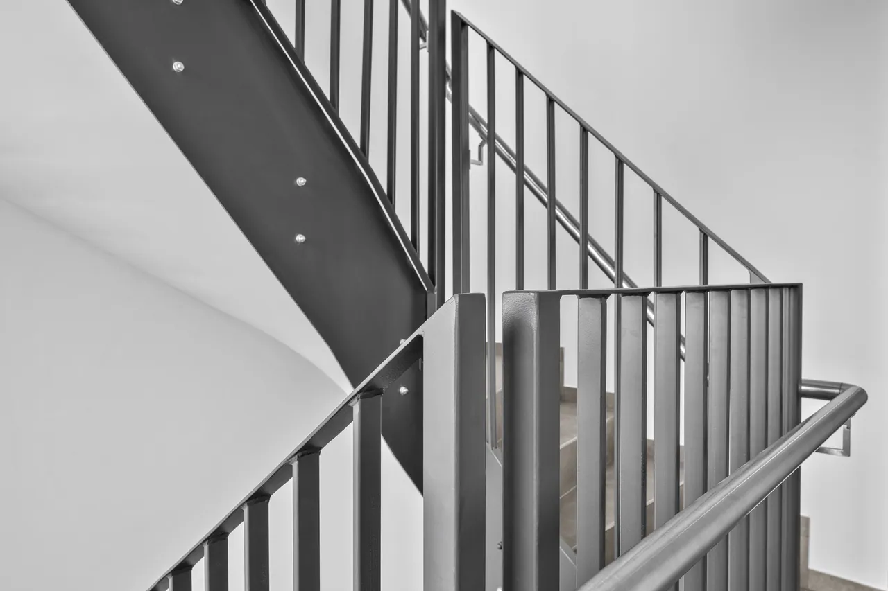 Nawrót balustrady przy podeście: słupek, pionowe pręty i wygięta poręcz ze stali nierdzewnej